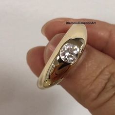 a hand holding a gold ring with a diamond in it's center and the band