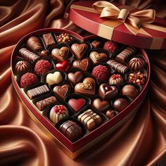 a heart shaped box filled with assorted chocolates on top of a satin cloth