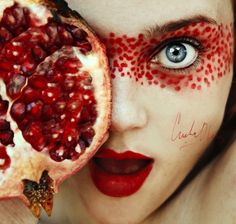 a woman with her face painted like a pomegranate holding a piece of fruit