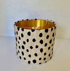 a black and white polka dot lamp shade with gold trim on the bottom, sitting on a table