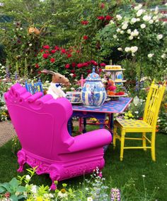 a pink chair sitting in the middle of a lush green field next to a table and chairs