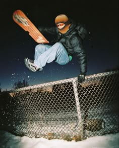 a man flying through the air on top of a snowboard in front of a fence