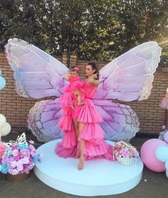 a woman in a pink dress standing next to a giant butterfly shaped float with balloons around her