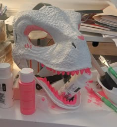 a white mask sitting on top of a table next to some paint bottles and markers