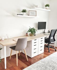 a desk with two laptops on it and some plants in the corner next to it