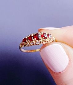 a woman's hand holding a gold ring with red stones