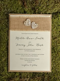 a wedding card with two hearts on it sitting in the grass next to some flowers