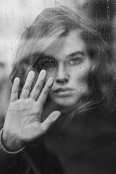 a woman holding her hand up to her face in front of a rain soaked window