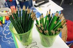 two green cups with pencils in them sitting on a table next to each other