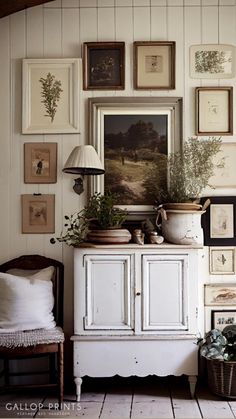 a white cabinet sitting in front of a wall filled with framed pictures and potted plants