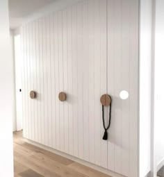 a white wall with three hooks on it and some wood flooring in front of it