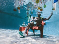 a man sitting in a chair under the water with bottles hanging from his legs and feet