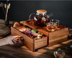 a wooden box with tea and snacks in it on a table next to other items