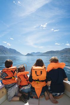 three children in life vests sitting on a boat looking out at the water and mountains