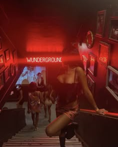 a group of women walking down stairs in a red lit room with neon signs on the walls