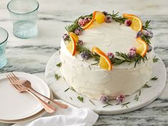 a white cake with orange slices and rosemary sprigs sits on a marble table