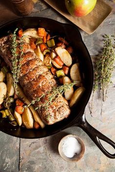 pork chops and potatoes in a skillet with apples, thyling sprigs and an apple on the side