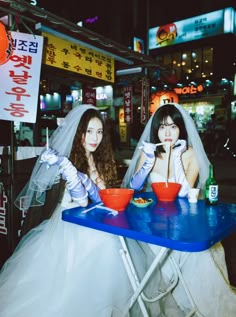 two brides sitting at a table with bowls of food