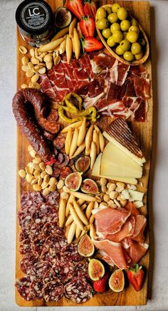 an assortment of meats and cheeses on a wooden platter with olives