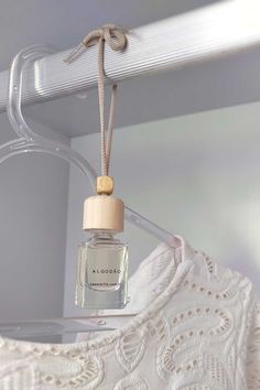 a white dress hanging from a hanger with a small bottle in front of it