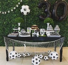 a table topped with soccer balls and desserts next to a wall covered in greenery