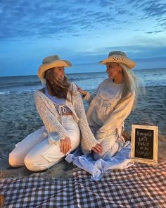 two women sitting on the beach next to each other