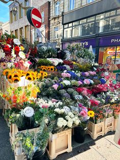 a bunch of flowers that are on display in front of a store with people walking by