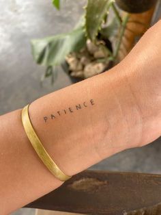 a woman's arm with the word patience written on it and a plant in the background