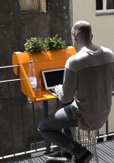 a man sitting at a table with a laptop on top of it and a planter in front of him