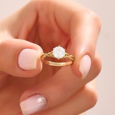 a woman's hand holding a gold ring with a white diamond on it,