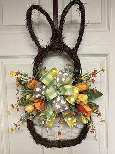 a wreath with flowers and bunny ears hanging on the front door to give it a festive look