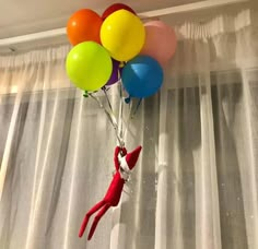 there is a red elf hanging from the ceiling with balloons attached to it's head