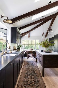 a kitchen with black cabinets and wooden beams on the ceiling, along with an area rug