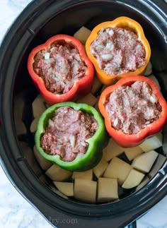 four peppers stuffed with meat and cheese in a slow cooker, ready to be cooked