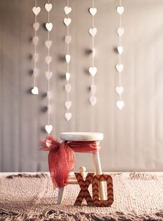 a small wooden stool with a bow on it and hearts hanging from the ceiling above