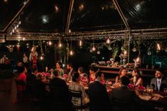 a group of people sitting around a table in a room with lights hanging from the ceiling