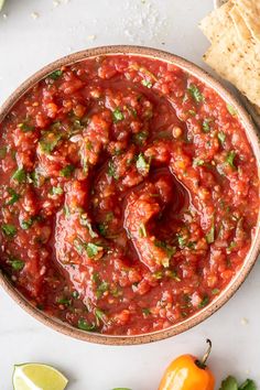 a bowl filled with salsa and tortilla chips next to it on a white surface