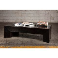 a coffee table with books on it in front of a brick wall and concrete floor