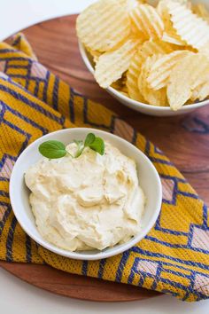 two bowls filled with dip and chips on top of a wooden tray