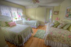 two beds in a room with yellow walls and wooden floors, one has pink flowers on it