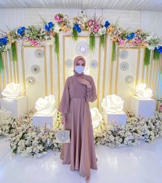 a woman wearing a face mask standing in front of a floral decorated stage with flowers