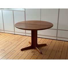 a round wooden table sitting on top of a hard wood floor next to a white wall