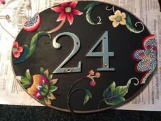 the number twenty four is decorated with flowers and leaves on a black plaque that reads, 24