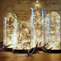 three glass jars filled with lights on top of a wooden table next to antlers