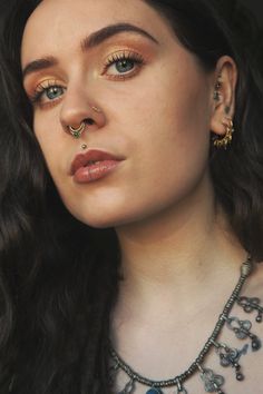 a close up of a person wearing a necklace and nose ring with piercings on it