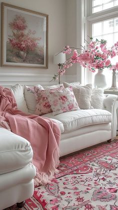 a living room with white furniture and pink flowers in vases on the window sill