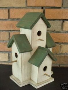 three wooden birdhouses with green roof tops on a table next to a brick wall