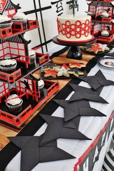 a table topped with cakes and cupcakes covered in black paper cranes on top of it