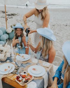 three women sitting at a table with hats on their heads and plates in front of them