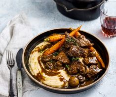 a bowl filled with meat, potatoes and carrots next to a glass of wine